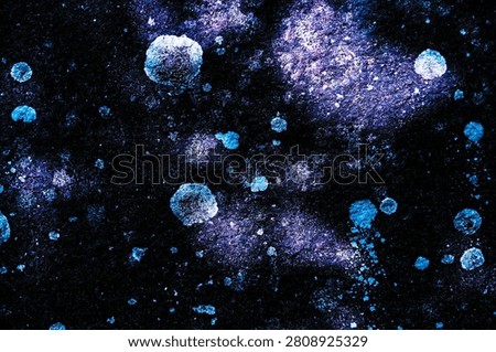 Creative cosmic abstract background featuring glowing blue and purple paint splatters over a dark textured stone canvas.