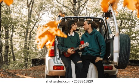 Creative couple of a man and a woman are sitting in the trunk of a car talking and playing the guitar in the autumn forest. - Powered by Shutterstock