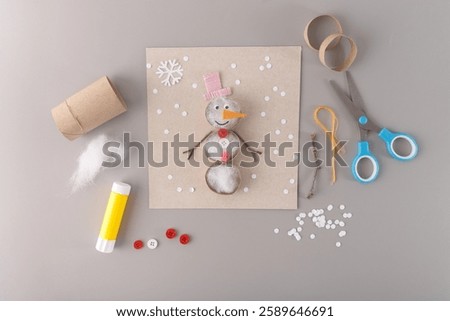 Creative craft project with a snowman made of cotton stuffing, pink hat, and buttons. Ideal for promoting holiday workshops, craft kits, or educational businesses for kids. top view