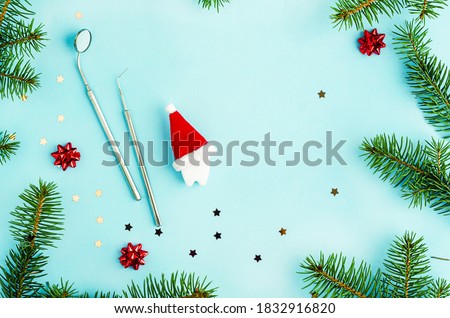 creative dental christmas and new year. mirror, probe and toy tooth in santa hat on year background with fir branches