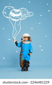 Creative design with drawn elements. Portrait of little boy, child in costume of astronaut over blue background. Planet doodles. Concept of imagination, childhood, creativity, dreams, ad