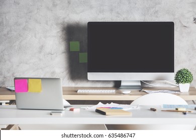 Creative Designer Desktop With Largeempty Computer Screen, Laptop With Stickers And Supplies. Shadow On Concrete Wall. Mock Up