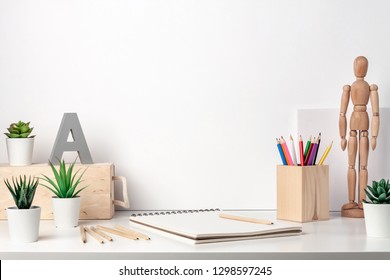 Creative desk by the white wall of the hipster with wooden accessories. Natural drawing space. Succulents, colored pencils, sketchbook and wooden figure of a man. Copy space for text - Powered by Shutterstock