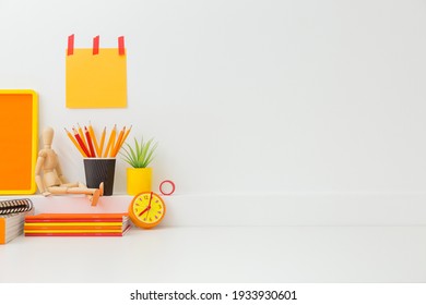 Creative desk in kids room with yellow frame mock up, plant and notebooks, note on the wall and many yellow and orange supplies.