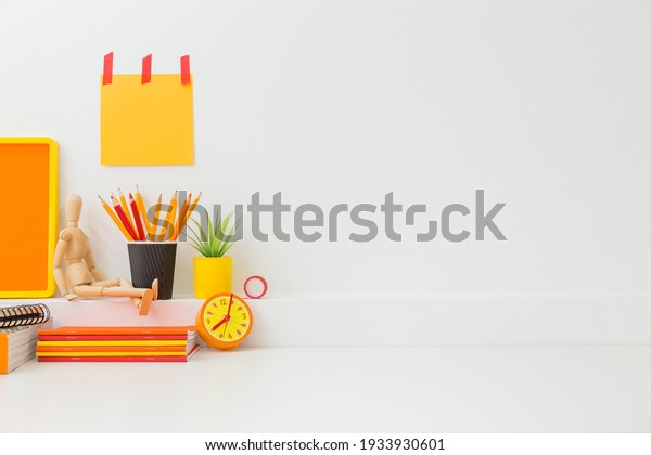 Creative desk in kids room with yellow frame\
mock up, plant and notebooks, note on the wall and many yellow and\
orange supplies.