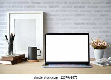 Creative desk workspace with blank picture frame poster, blank screen laptop for graphic display montage