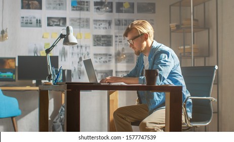 Creative Developer Works On A Laptop In His Studio. Designing Apps, Games And Doing Video Editing. In The Background Modern Sunny Loft Office With Project Storyboard And Concepts Covering The Wall