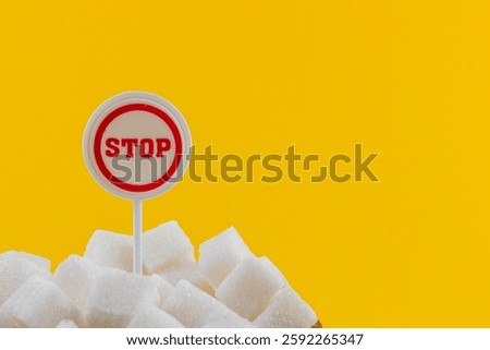 A creative display features a bold stop sign amidst piles of sugar cubes against a vibrant yellow background, emphasizing the message of reducing sugar consumption for better health.