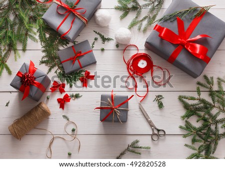 Creative diy hobby. Giftwrapping. Wrapping modern christmas present, boxes in stylish gray paper with red ribbon. Top view of messy white wooden table with fir tree branches, decoration of gift.