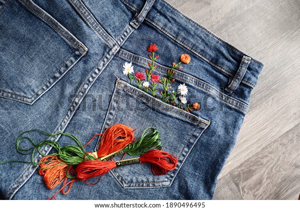 Creative DIY project, hand embroidery\
at home on jeans, creative hobby, clothes recycle, floral\
embroidery design, colorful threads, embroidery\
needle