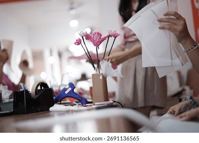 ​A creative DIY workshop in session. People are learning to make beautiful, handmade flower bouquets from pink pipe cleaners on a wooden table.