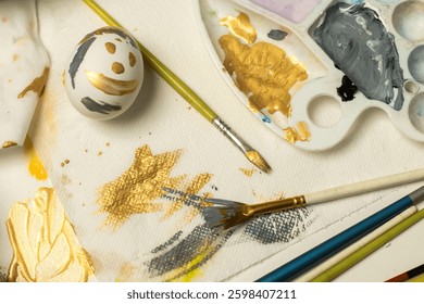 Creative Easter egg painting setup with a palette, paintbrushes, and a decorated egg with gold and black smiley face on tissue paper, perfect for holiday DIY crafts.