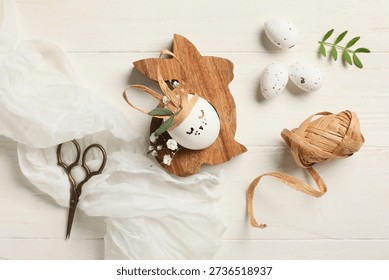 Creative Easter eggs with rabbit and supplies on white wooden background