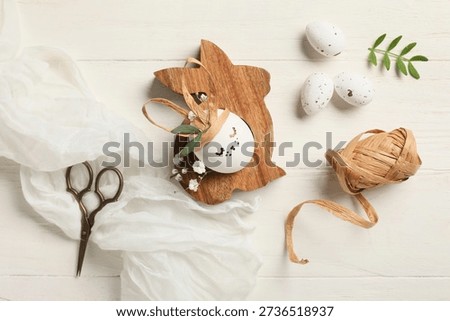 Creative Easter eggs with rabbit and supplies on white wooden background