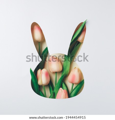 Creative Easter layout with fresh tulip flowers and leaves on bright white and beige paper background. Spring natural concept. Bunny shape Easter holiday minimal composition. Flat lay, top view.