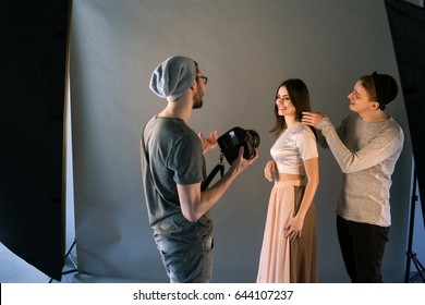 Creative fashion team work with model in studio. Professional stylist and photographer communicate with cheerful woman on photoshoot