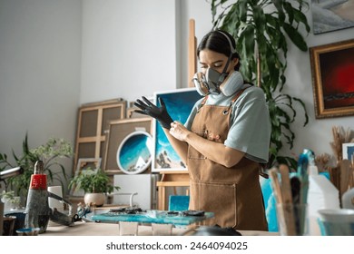 Creative female artist wearing respirator, latex gloves works with epoxy resin, crafting pieces on canvas in art studio. Manufacturing process of products made of liquid decorating material  - Powered by Shutterstock