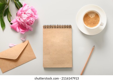Creative female mock up with craft sketchbook, coffee cup, pink peony flower on gray background. Copy space. Top view, flat lay.