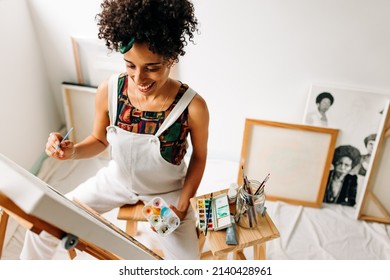 Creative female painter working on a new painting. Happy young woman smiling cheerfully while drawing on a canvas in her art studio. Cheerful young female painter working in a workshop. - Powered by Shutterstock