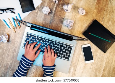 Creative Female Person Working On Laptop Computer In The Office, Top View Of Hands Typing Keyboard On Desk With Smartphone And Papers Scattered Around