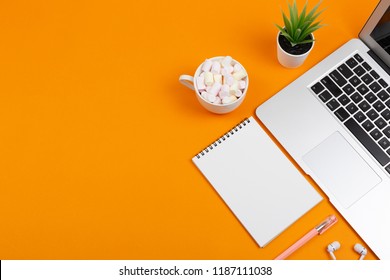 Creative feminine workplace with stationery supplies, laptop and earphones. Cup with colorful marshmallows. Freelance, work at home or blogging concept. Bright colors. Copy space for your text.