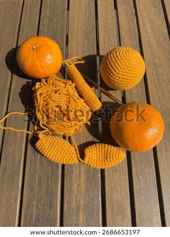 Creative flat lay of bright orange yearn and crochet pieces arranged beside fresh oranges on a wooden table under natural sunlight. It highlights harmony between handmade crafts and nature.