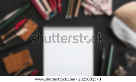 A creative flat lay composition featuring a blank white notebook surrounded by various art supplies like pencils, brushes, and erasers on a dark surface.
