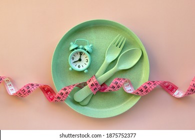 Creative flat lay composition with plate, alarm clock, spoon, fork and measuring tape on pink background. Intermittent fasting, ketogenic, diet concept.  Flat lay, copy space.
 - Shutterstock ID 1875752377