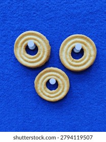 Creative flat lay composition of three ring biscuits arranged on a vibrant blue felt cloth texture background, featuring white plastic pins in the center holes.