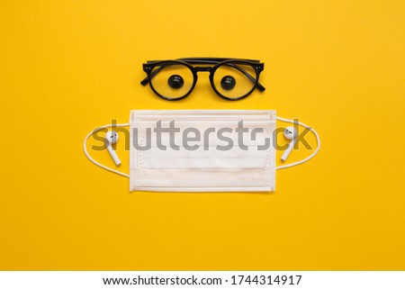 Creative flat lay concept with black glasses, headphones and mask on yellow background. A creative person during a epidemic.