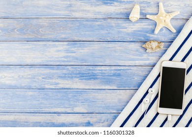 Creative flat lay concept of summer travel vacations. Top view of beach towel smartphone seashells starfish on pastel blue wooden planks background with copy space mockup template for text