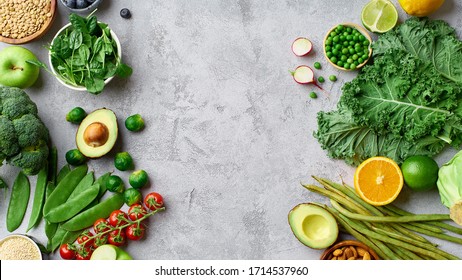 Creative flat lay with healthy vegetarian food ingredients. Raw food concept with avocado, kale and tomatoes. Organic fruits and vegetables on concrete background, copy space. Clean eating selection