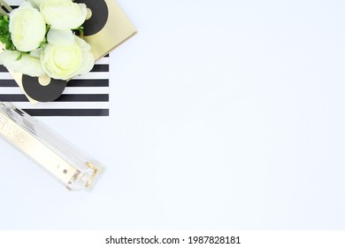 Creative flat lay photo of workspace desk with flowers,  gold staple and striped notebook on white background