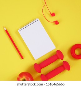 Creative flat lay sport and fitness concept. Top view of dumbbells, headphones, hand expander, apple, notebook and pencil on a yellow background with space for text. The size is square.