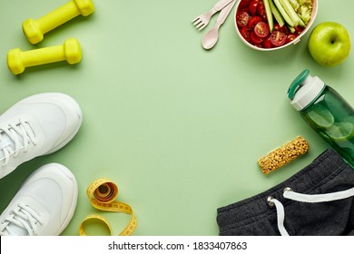 Creative flat lay of sport and fitness equipments. Women's white sneakers, water bottle, sportswear, dumbbells and lunchbox with healthy vegetable salad, on light green background.: stockfoto