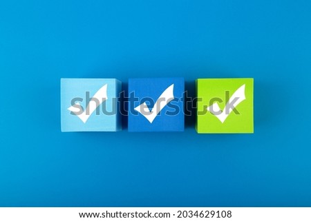 Creative flat lay with three checkmarks close up on blue and green toy cubes in the middle of blue background. Concept of questionary, checklist, to do list, planning or business plans
