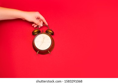 Creative flat lay top view concept of a female hand holding a vintage alarm clock on bright red color paper background with copy space in minimal style, template for text