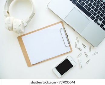 Creative flat lay of workplace with smartphone, clipboard, laptop and headphone on white background, copy space, minimal style.