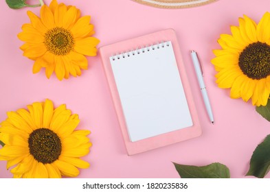 Creative flat lay of workspace desk, notepad and sunflower on pink background