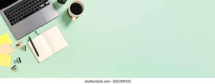 Creative flat lay of workspace desk. Top view office desk with laptop, coffee cup and open mockup black notebook on green background. Panoramic banner with copy space for text and Advertising area.