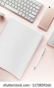 Creative flat lay workspace with minimal style. Modern desk with computer, smartphone, magazine, notebook, pencil and tapeline on a pastel pink background, top view