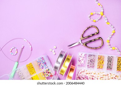 Creative flatlay of different pearl beads with tools for making jewelry, wire string and scissors isolated on pink background.