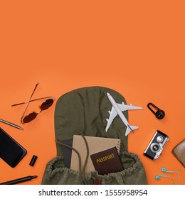 Creative Flatlay Of Traveler's Accessories With Passport, Books Of Travel Plan, Mobile Phone, Camera, Backpack And Airplane Toy Isolated Orange Background With Empty Space,Tropical Travel Concept