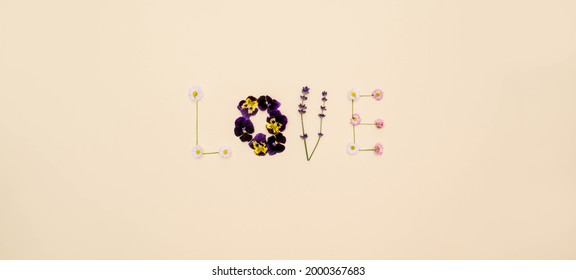 Creative flowers composition. Word love made of daisies and lavender flowers on bright yellow background. Flat lay, top view.