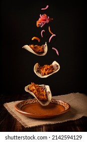 Creative food image of Mexican Tacos de Cochinita Pibil and onion with habanero chili falling on traditional mexican clay dish. Levitation photography.
