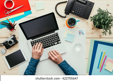 Creative Freelancer Working At Desk In His Office, He Is Typing With A Laptop, Top View