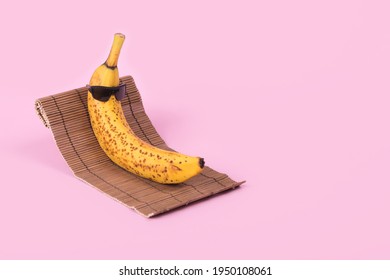 Creative fun idea with a banana in sunglasses lying on a sun bed on a pastel pink background. Minimal travel concept, summer stylish tropical fruit. Summertime color mood.Fashion and trend.Copy space.