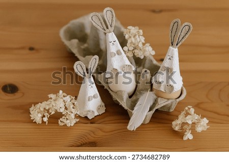Creative funny DIY for Easter. Sweet bunny from egg carton packaging. Eco friendly simple craft for children. Holiday cute rabbit and eggs in paper egg packaging with flowers and feather on wooden natural background. Reuse recycle idea, rustic home decor for Easter.