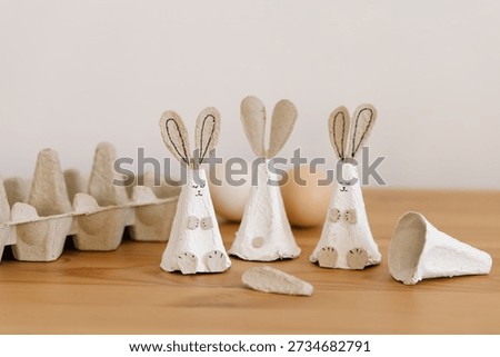 Creative funny DIY for Easter. Sweet bunny from egg carton packaging. Eco friendly simple craft with details for children. Side view of holiday cute rabbit and eggs in paper egg packaging on wooden natural background. Reuse recycle idea, rustic home decor for Easter.