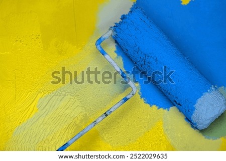 Creative graphic concept of paint roller applying fresh blue paint onto the yellow color concrete wall. Process of home renovation, improvement and makeover. Copy space.